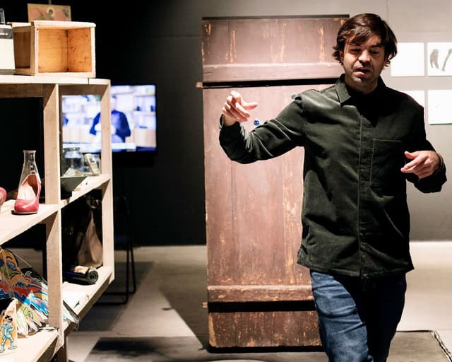 Francisco Martínez giving a gallery talk beside a wooden cabinet and shelf of objects